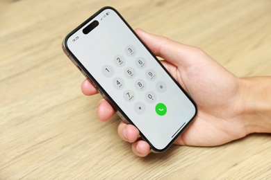 Photo of Man holding smartphone with keypad at wooden table, closeup