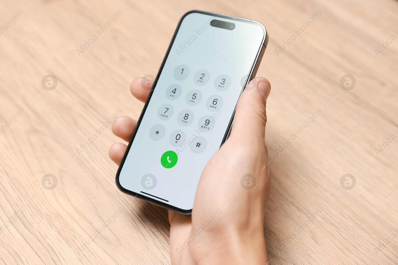 Photo of Man holding smartphone with keypad at wooden table, closeup