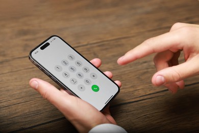 Photo of Man dialing number on smartphone at wooden table, closeup