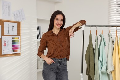 Photo of Fashion designer near rack with clothes in workshop