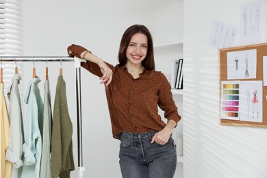 Photo of Fashion designer near rack with clothes in workshop