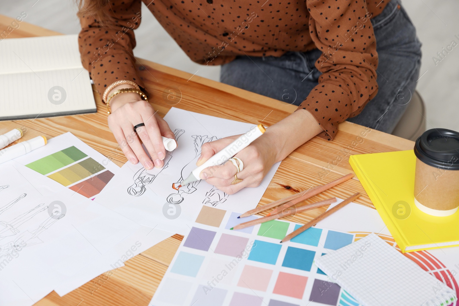 Photo of Fashion designer drawing sketch of clothes at wooden table in workshop, closeup