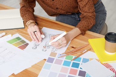 Photo of Fashion designer drawing sketch of clothes at wooden table in workshop, closeup