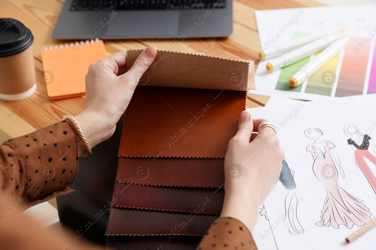 Photo of Fashion designer choosing fabric among colorful samples at wooden table in workshop, closeup