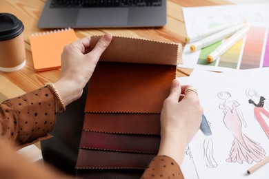 Photo of Fashion designer choosing fabric among colorful samples at wooden table in workshop, closeup