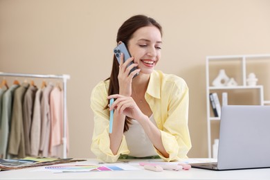 Photo of Fashion designer talking on smartphone at white table in workshop