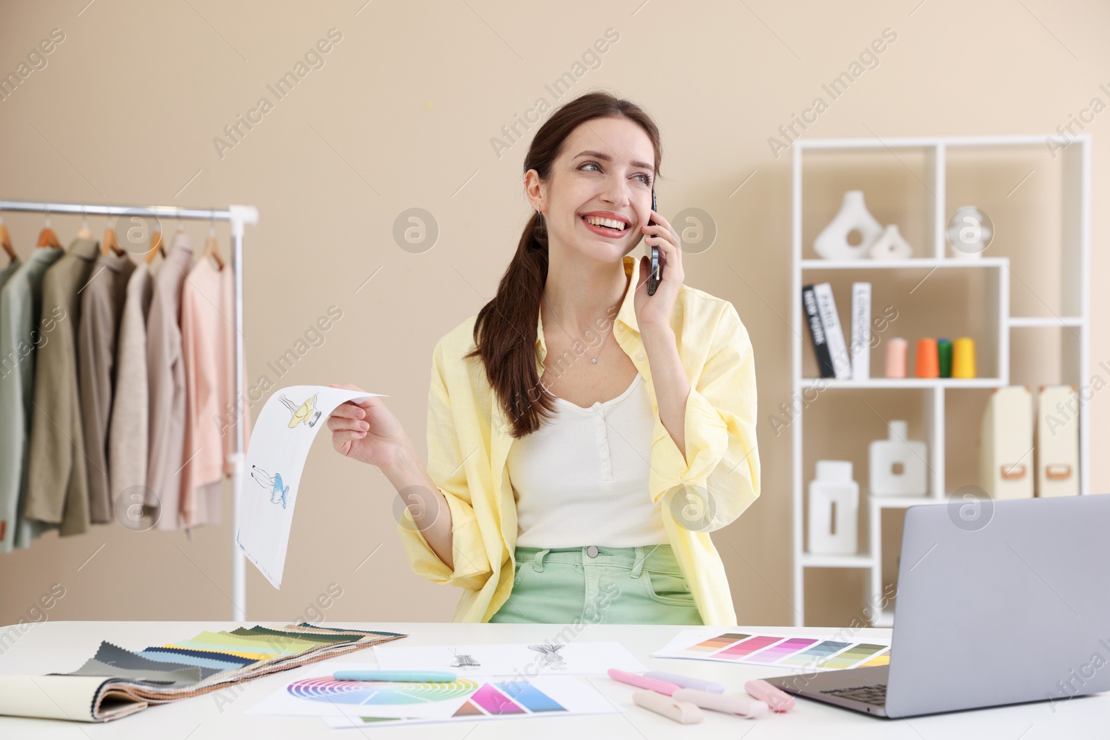 Photo of Fashion designer talking on smartphone at white table in workshop