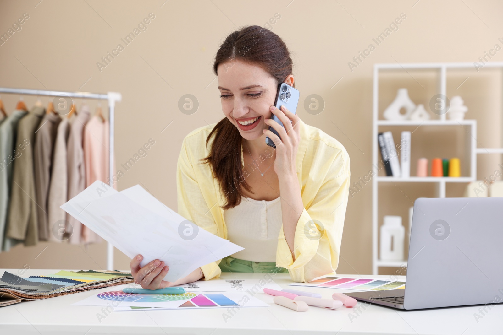 Photo of Fashion designer talking on smartphone at white table in workshop