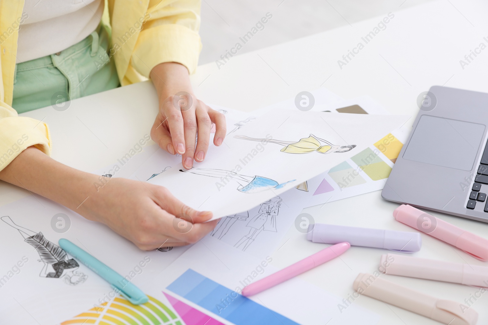 Photo of Fashion designer with sketch of clothes working at white table in workshop, closeup