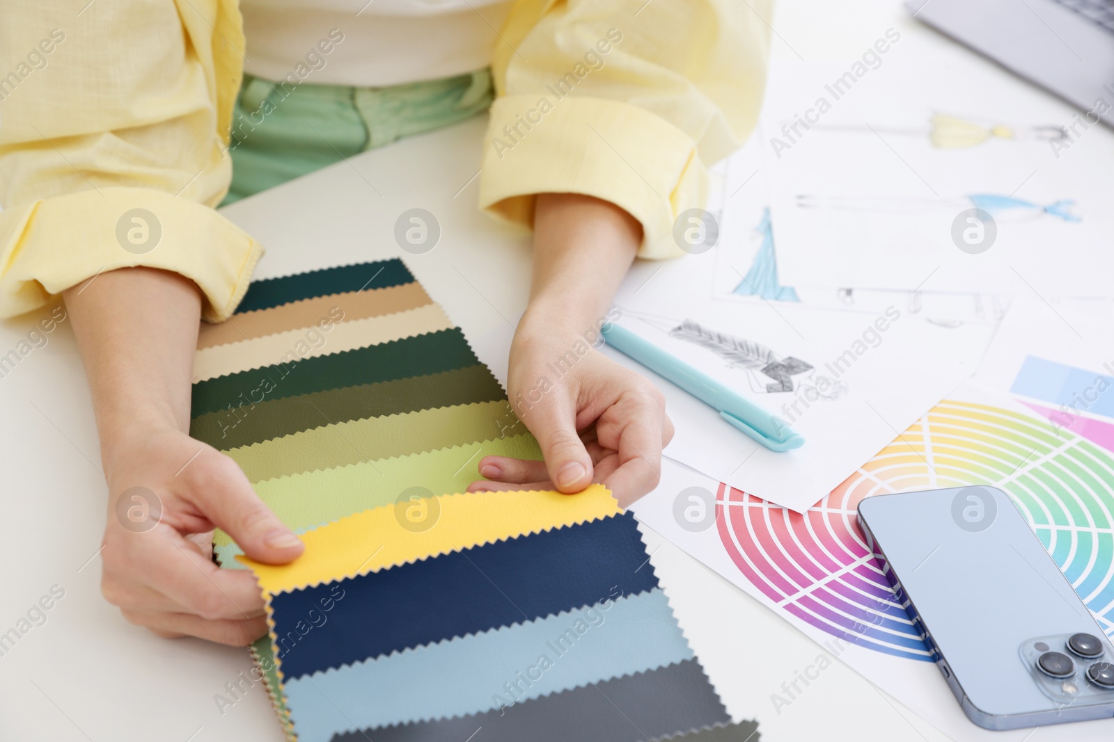 Photo of Fashion designer choosing fabric among colorful samples at white table in workshop, closeup