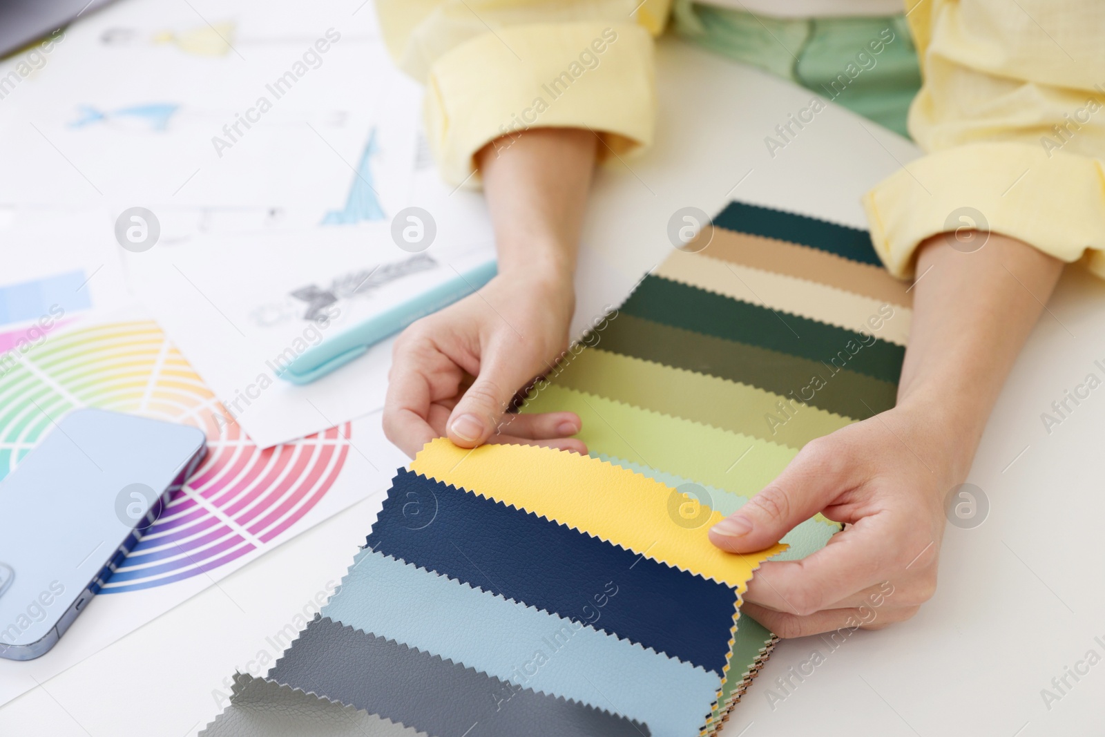 Photo of Fashion designer choosing fabric among colorful samples at white table in workshop, closeup