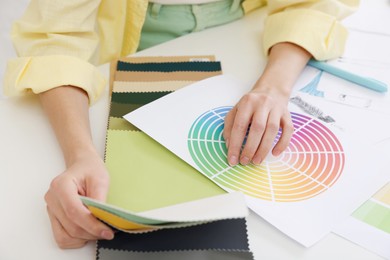 Photo of Fashion designer with color palette choosing fabric among different samples at white table in workshop, closeup