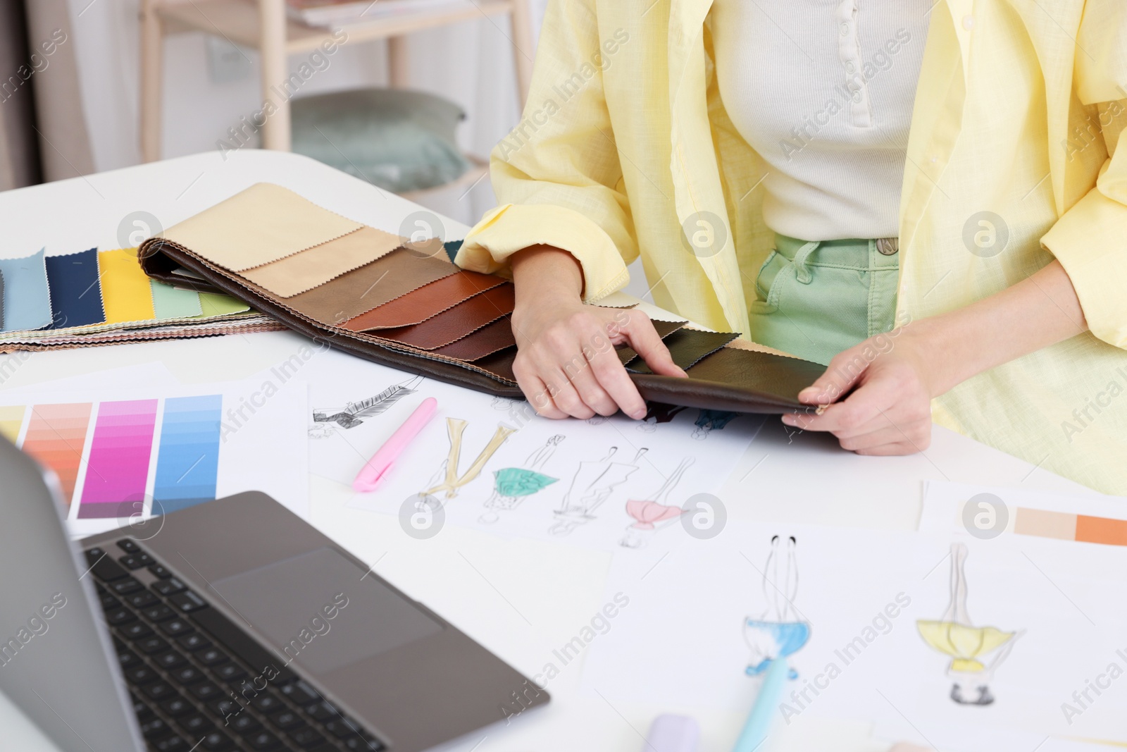 Photo of Fashion designer choosing fabric among colorful samples at white table in workshop, closeup