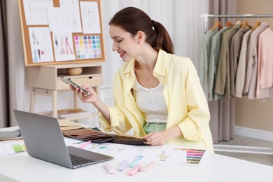 Photo of Fashion designer using smartphone at white table in workshop