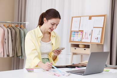 Fashion designer using smartphone at white table in workshop