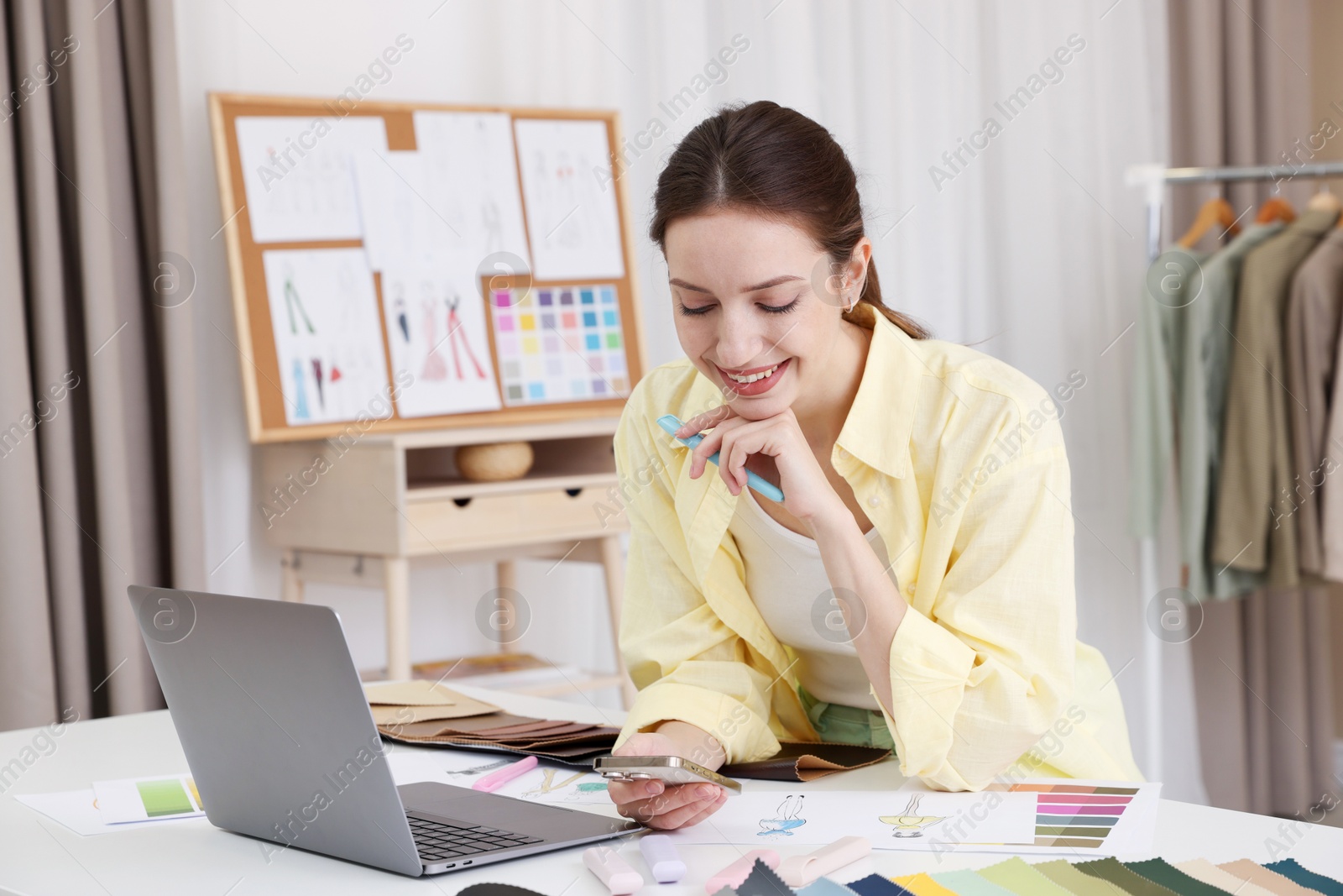 Photo of Fashion designer using smartphone at white table in workshop