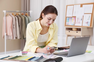 Photo of Fashion designer using smartphone at white table in workshop