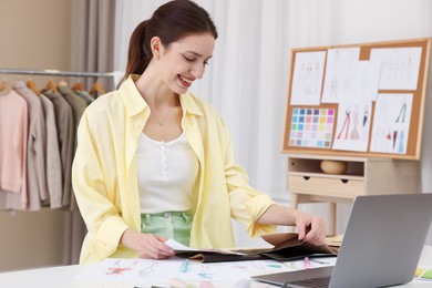 Photo of Fashion designer choosing fabric among colorful samples at white table in workshop