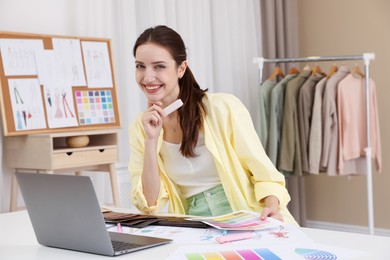 Photo of Fashion designer with sketches of clothes and color palettes working at white table in workshop