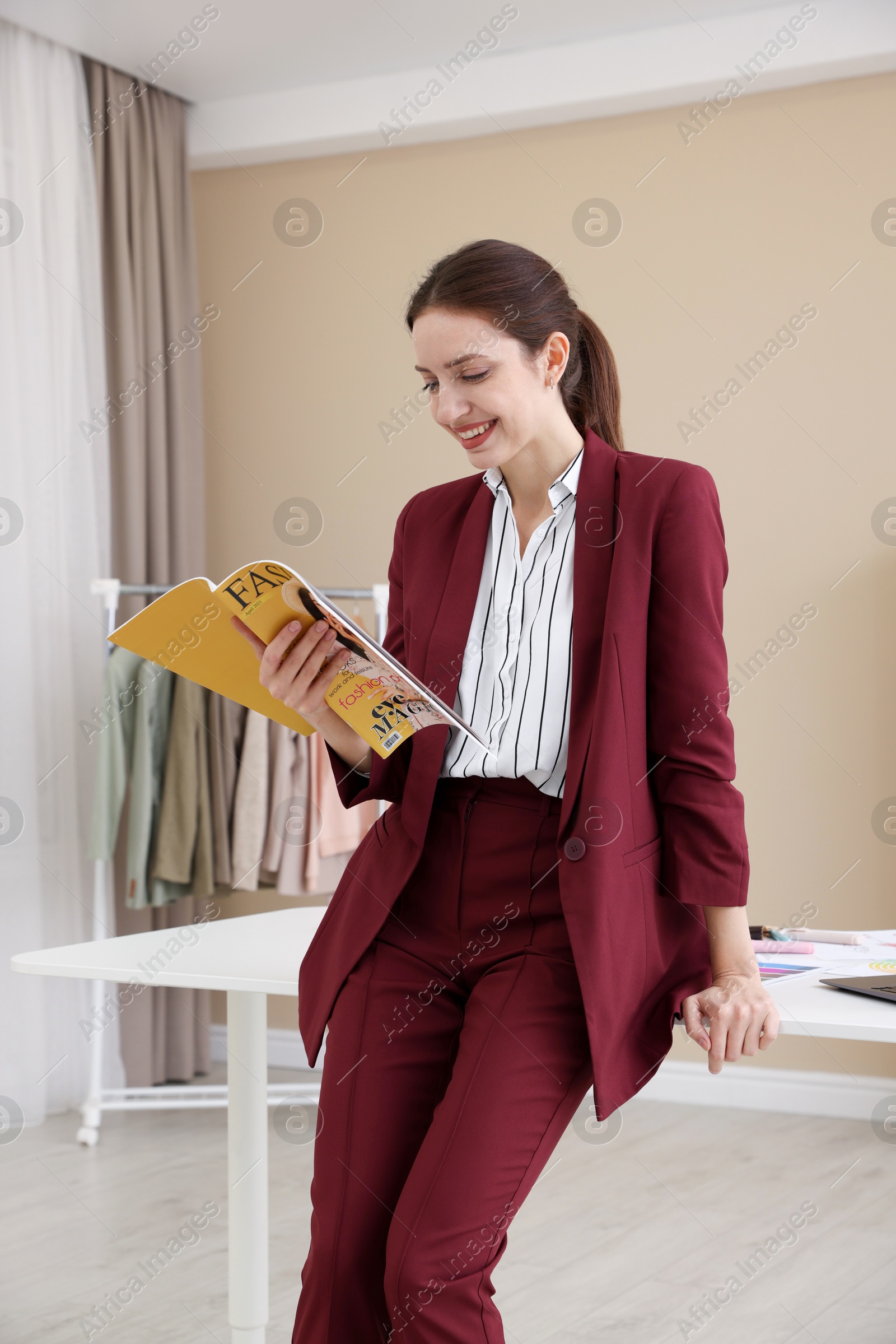 Photo of Fashion designer reading magazine near table in workshop