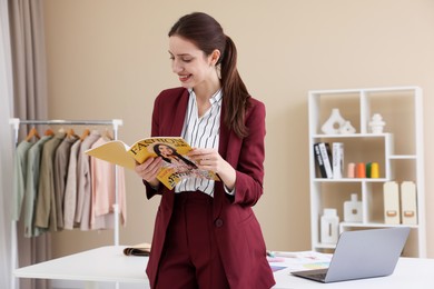 Photo of Fashion designer reading magazine near table in workshop