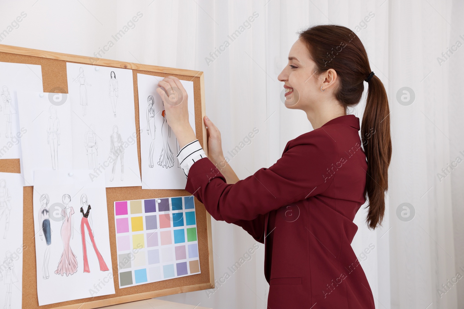 Photo of Fashion designer pinning sketch of clothes to corkboard in workshop