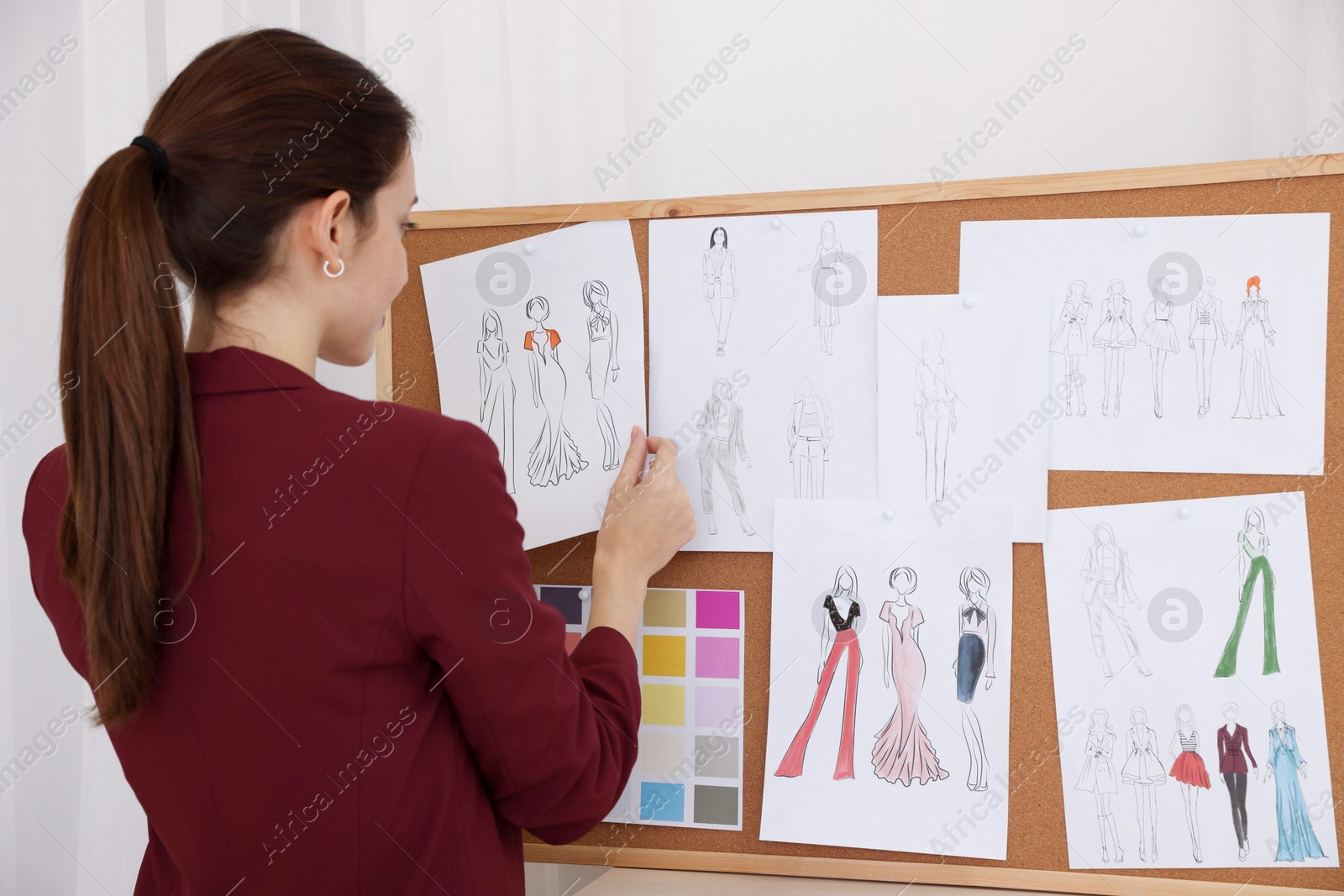 Photo of Fashion designer pinning sketch of clothes to corkboard in workshop