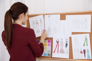 Photo of Fashion designer pinning sketch of clothes to corkboard in workshop