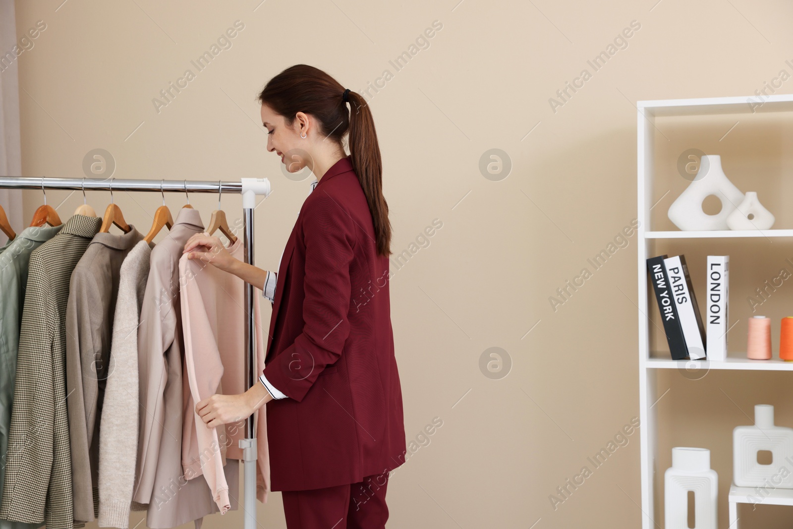 Photo of Fashion designer near rack with clothes in workshop