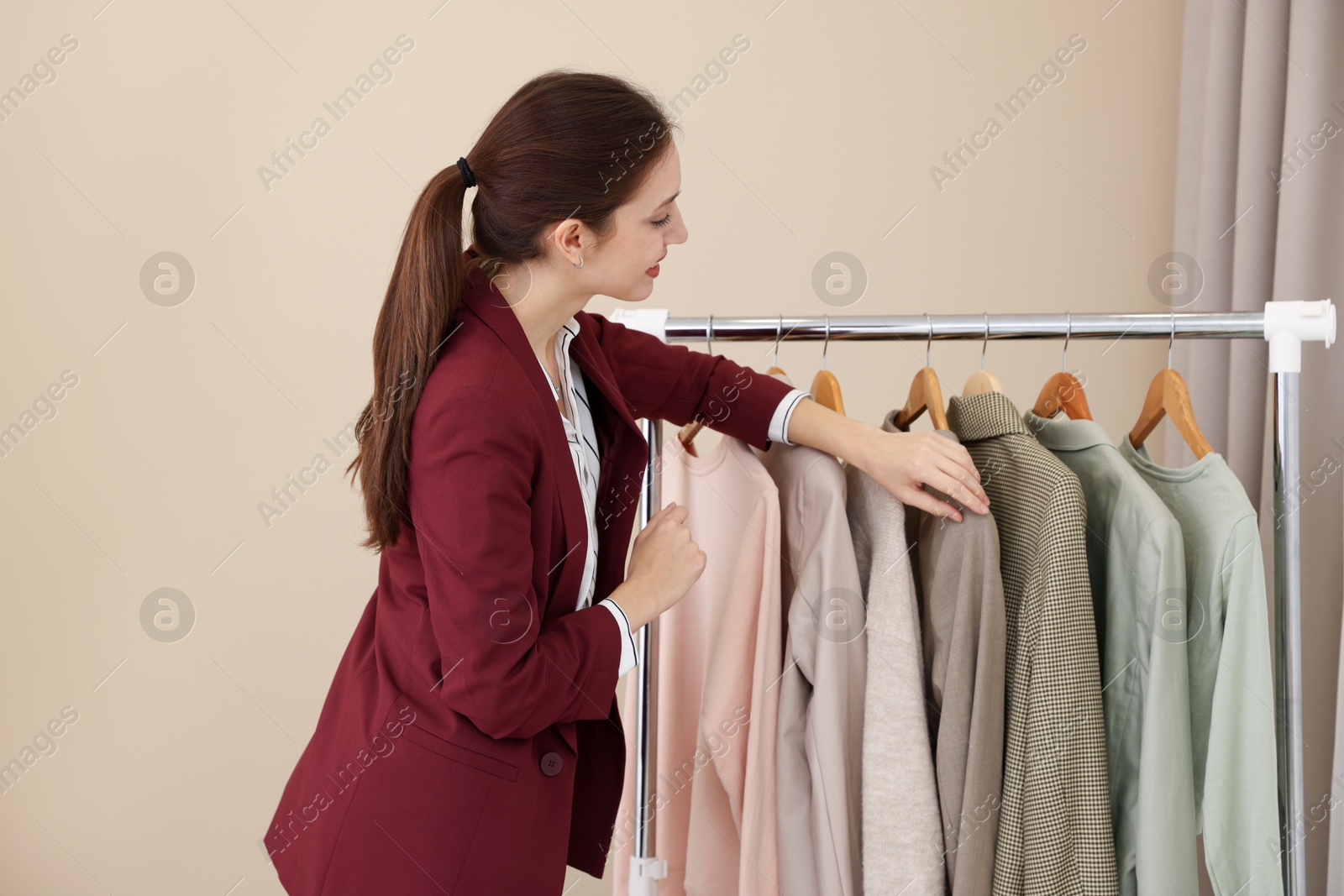 Photo of Fashion designer near rack with clothes in workshop