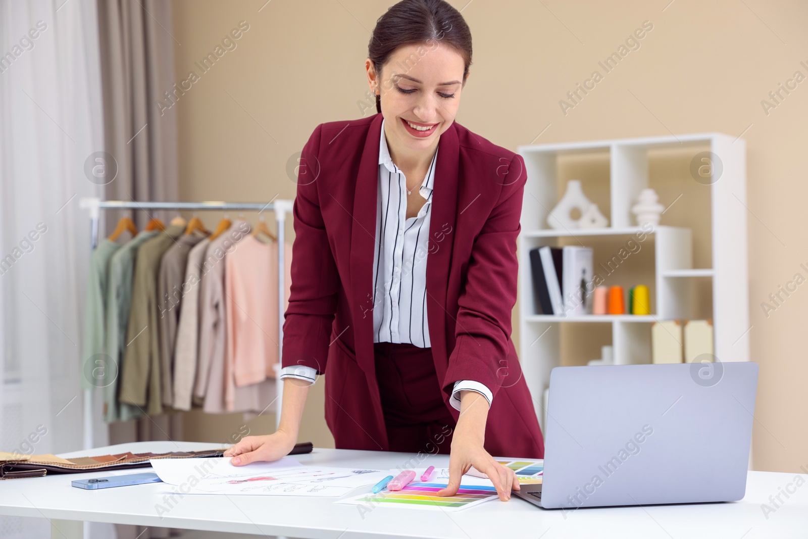 Photo of Fashion designer with sketches of clothes and color palettes working at white table in workshop