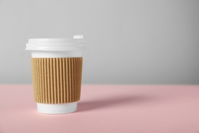 Photo of Paper cup with lid on pink table against grey background, closeup. Mockup for design