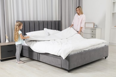 Photo of Little girl helping her mother making bed at home