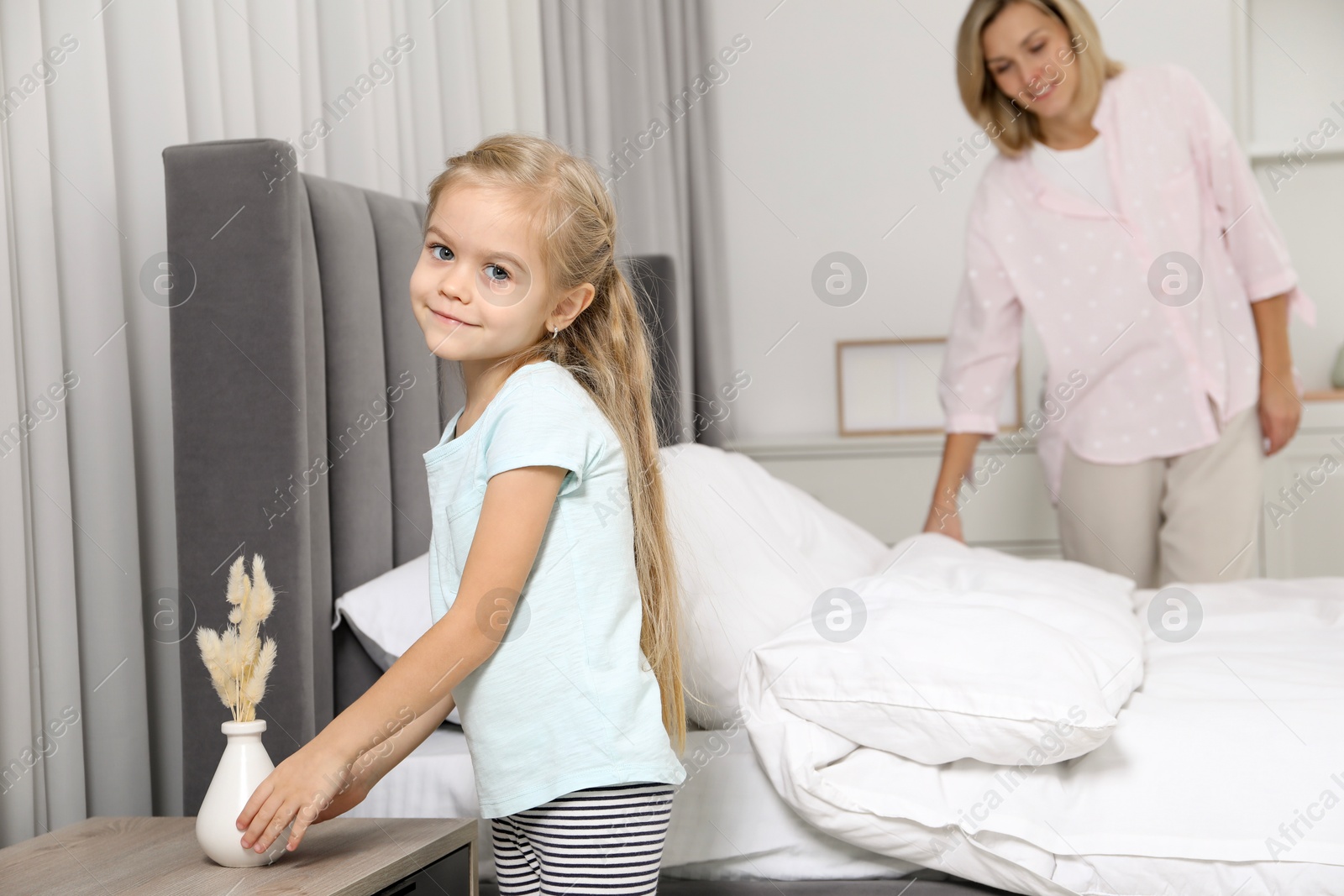 Photo of Little girl helping her mother making bed at home