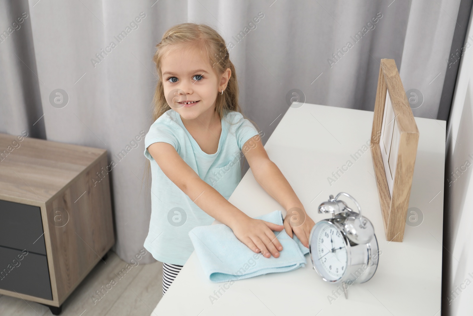 Photo of Little helper. Cute girl wiping dust at home