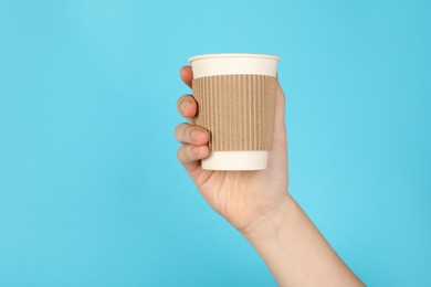 Photo of Woman holding paper cup on light blue background, closeup. Mockup for design