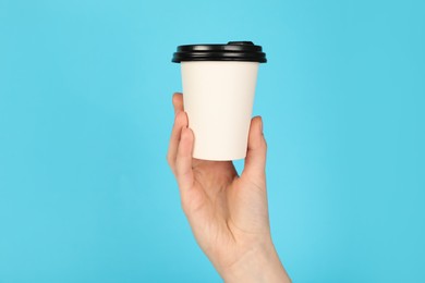 Photo of Woman holding paper cup on light blue background, closeup. Mockup for design