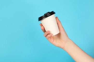 Photo of Woman holding paper cup on light blue background, closeup. Mockup for design