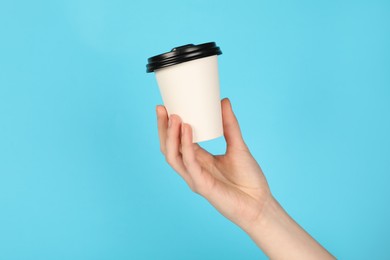Photo of Woman holding paper cup on light blue background, closeup. Mockup for design