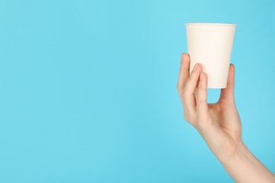 Photo of Woman holding paper cup on light blue background, closeup. Mockup for design