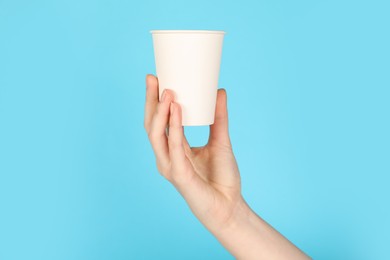 Photo of Woman holding paper cup on light blue background, closeup. Mockup for design