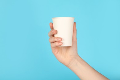 Photo of Woman holding paper cup on light blue background, closeup. Mockup for design