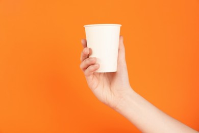 Photo of Woman holding paper cup on orange background, closeup. Mockup for design