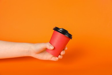 Photo of Woman holding paper cup on orange background, closeup. Mockup for design