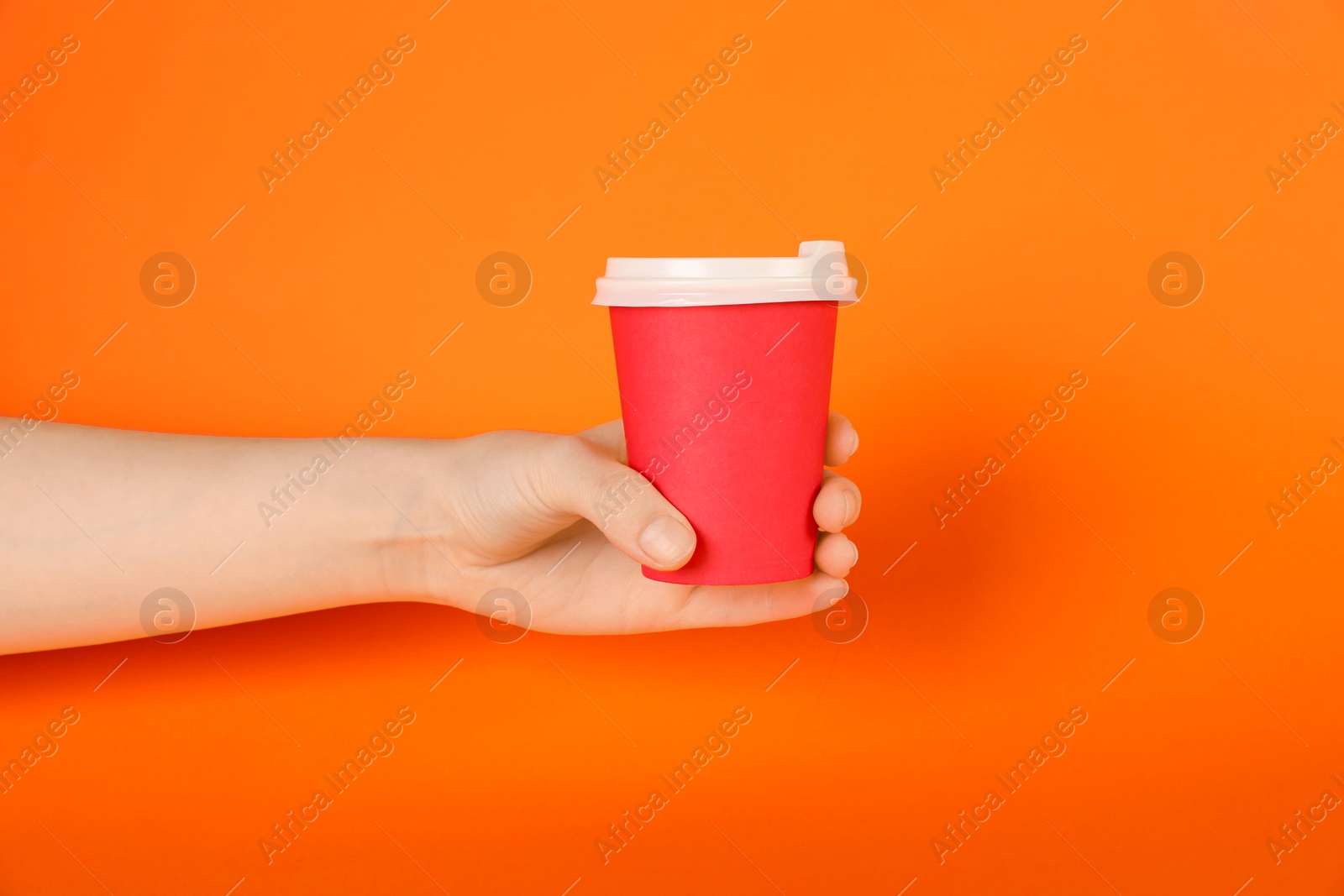Woman holding paper cup on orange background, closeup. Mockup for design Photo of Woman holding paper cup on orange background, closeup. Mockup for design