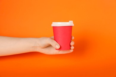 Photo of Woman holding paper cup on orange background, closeup. Mockup for design