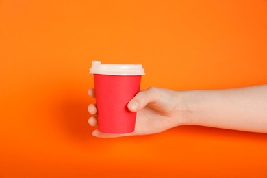 Photo of Woman holding paper cup on orange background, closeup. Mockup for design
