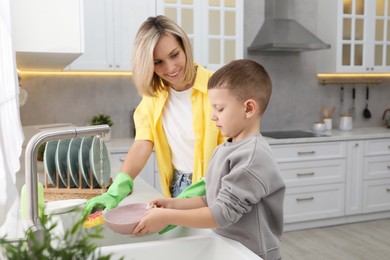 Photo of Little boy helping his mother washing dishes at home