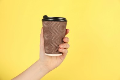 Photo of Woman holding paper cup on yellow background, closeup. Mockup for design