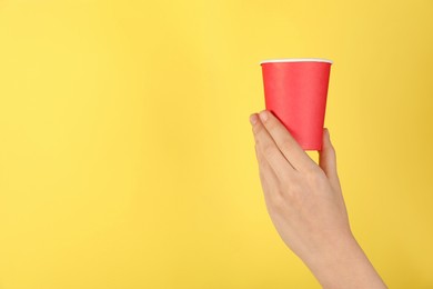Photo of Woman holding paper cup on yellow background, closeup. Mockup for design